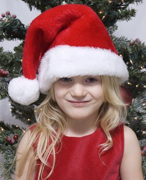 Young girl wearing a santa hat with christmas tree behind her