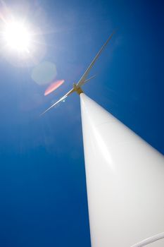 A wind turbine and the sun against a deep blue sky.  Image has heavy lens flare from the sun.