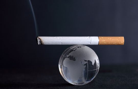 Conceptual balance: smoking cigarette lying on glass globe on dark background