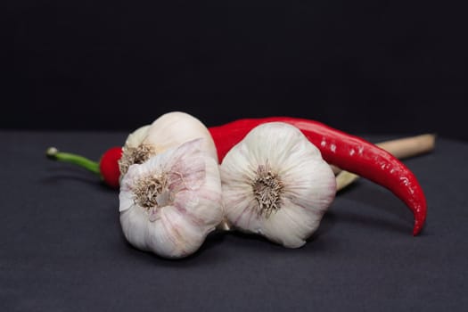 Few heads of garlic and one red chili pepper on dark background