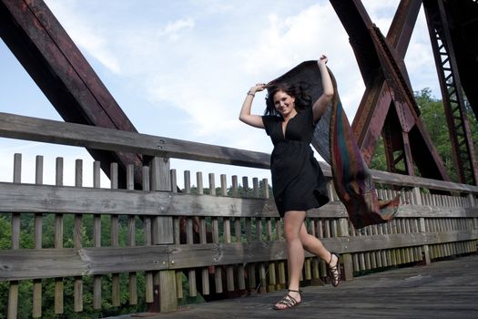 A carefree brunette woman running along a bridge with a scarf blowing in the breeze.