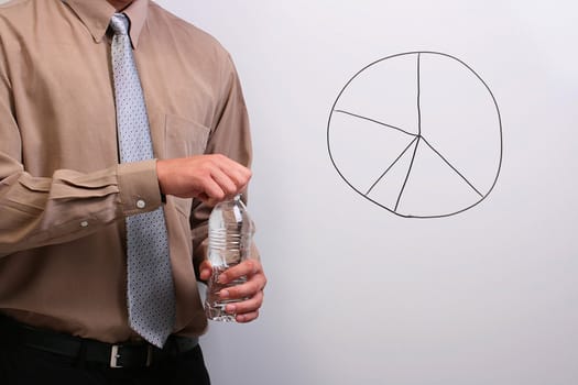 Man in a shirt and a tie opening a bottle of water while standing next to a drawing of a pie chart.