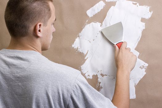 Caucasian man plastering a brown wall with a pallet.