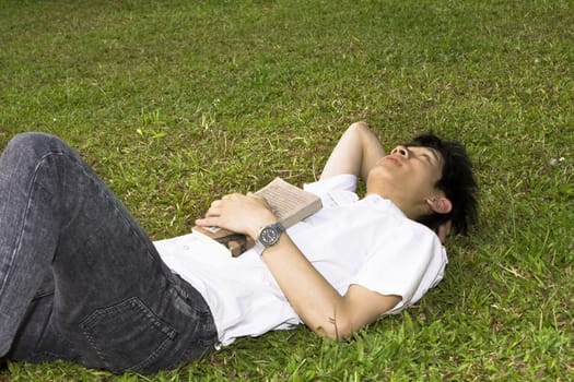 asia man relax on the grass and holding a book