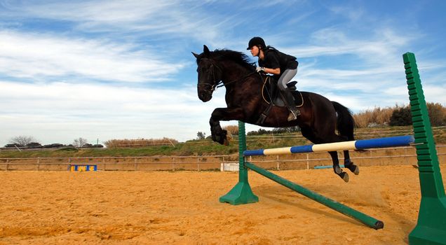 a young teenager and her black stallion in a training of jumping