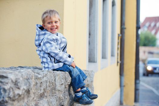 Cute little boy sits near the old house on a city street. Germany