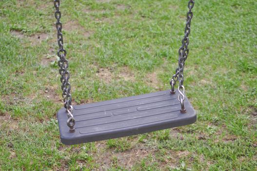 A swing suspended on chains in a playground on the grass