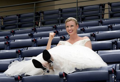 Model wearing wedding gown cheering in a baseball stadium.