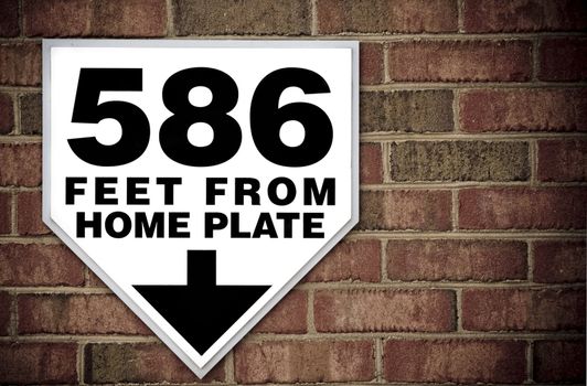 Stadium sign against a brick wall displaying distance to home plate with copy space.
