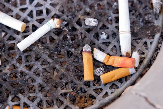 A dirty ashtray with smoked cigarette filters and butts with lipstick on them