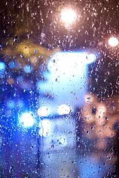 A full frame shot of a window looking outside towards the city lights while its raining, focus is on the rain drops.