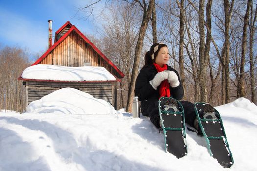 Snowshoeing in winter. Woman on snowshoes resting from hiking in beautiful winter forest. Cabin in the background. From Quebec, Canada.