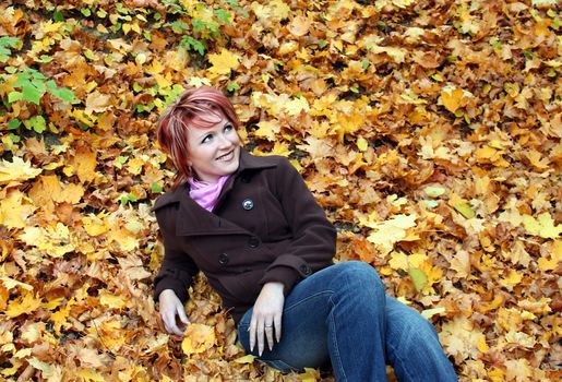 Young pretty woman lies in yellow leaves in park