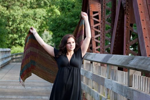 A carefree brunette woman running along a bridge with a scarf blowing in the breeze.