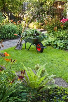 Evening after work in summer garden with wheelbarrow, shovel and rake - vertical