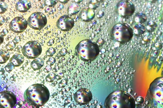 Close up view of many colorful and bright drops of water on a shiny surface.