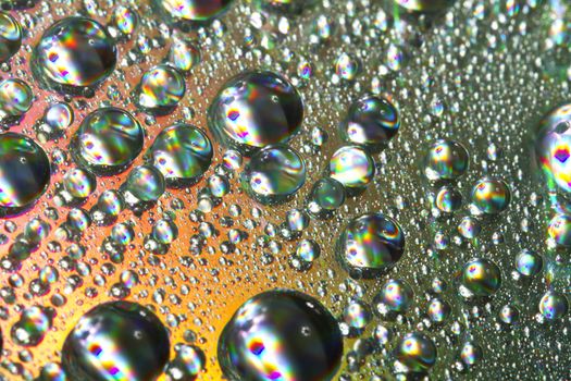 Close up view of many colorful and bright drops of water on a shiny surface.