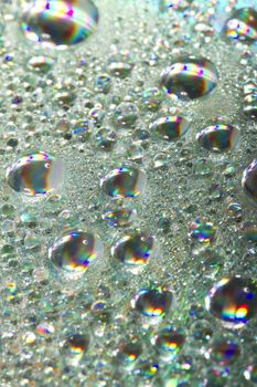 Close up view of many colorful and bright drops of water on a shiny surface.