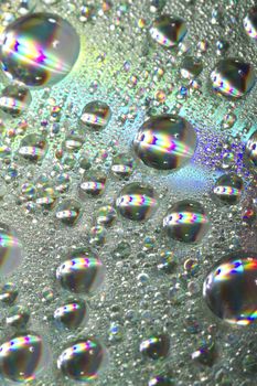 Close up view of many colorful and bright drops of water on a shiny surface.