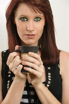 A beautiful female with vivid green eyes drinking tea or coffee.