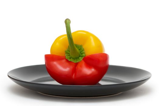 Red and yellow pepper on a black plate and a white background