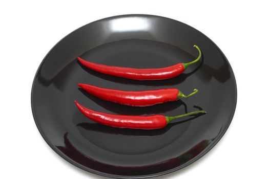 Three red chili peppers on a black plate