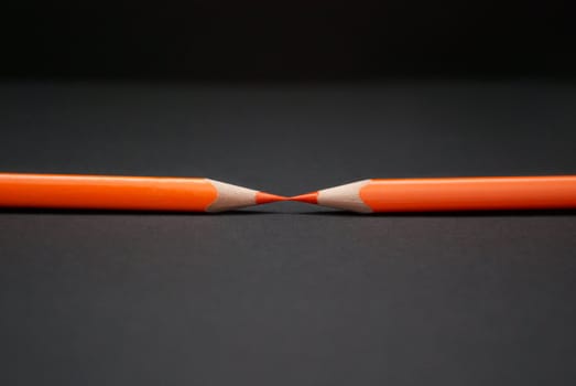 Two orange pencils on a black background