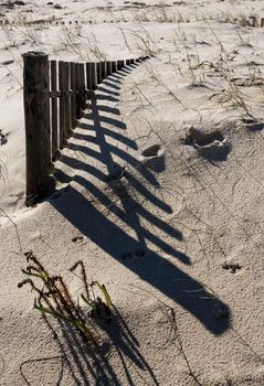 View of a section of a fence buried on the sand making a shadow.