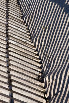 View of a section of a fence buried on the sand making a shadow.