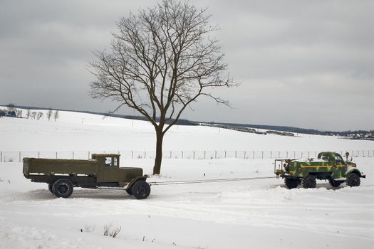 two old trucks in winter road. Car on a tow