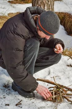 The young man kindles a fire in winter wood