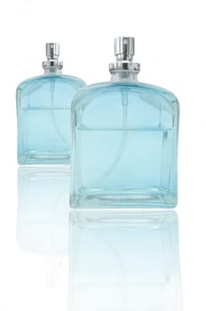 Low level capturing two glass blue perfume bottles arranged over white and reflecting into foreground
