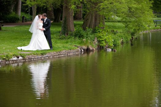 Bride and groom in the park kissing while they are reflected in the pond