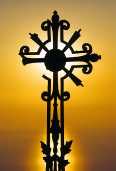 wrought iron cross in cemetery back lit by setting sun