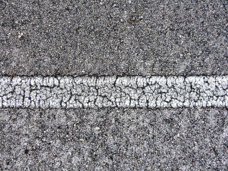 Straight white line view of an asphalt road with many cracks.