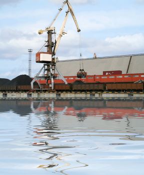 Container cranes for loading and unloading freight trains in Latvian port. Reflection over water.