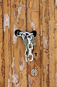 Close up view of a worn textured wooden door detail with chained lock.