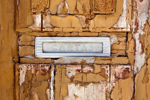 Close up view of a worn textured wooden door detail with mailbox opening.