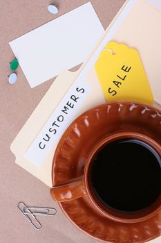 A manila customers folder laying next to a cup of coffee and office supplies. Add your text to the business card.