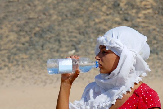 teen girl tourist drinking water in egyptian kerchief in desert
