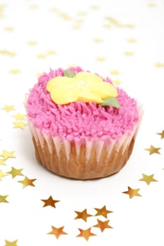 A pink frosted cupcake surrounded by star confetti.