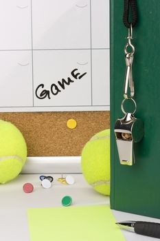 A silver whistle on a green notebook next to tennis balls and a calendar with the date of the game on it.