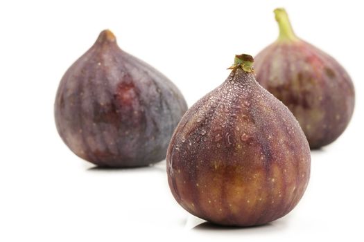 wet fig in front of two figs on white background