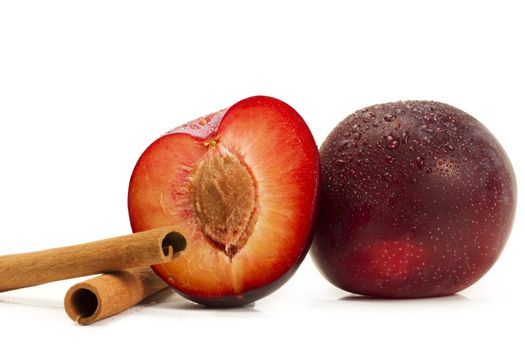 wet plum and a half and two cinnamon sticks on white background