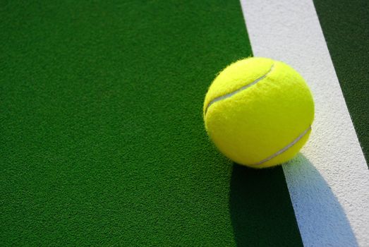 Close up of a yellow tennis ball resting on the white foul line