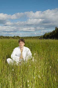 The young man meditates while sitting in a field