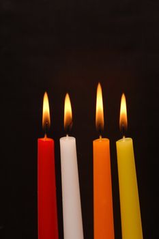 Set of four colored lighting candles on dark background