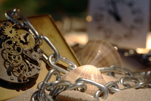 Abstract background with old clock mechanism standing on sand with stones and shells and chain