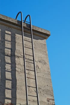 Steel ladder up concrete wall with blue sky background