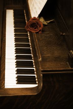 A rose rests on a piano with sheet music.